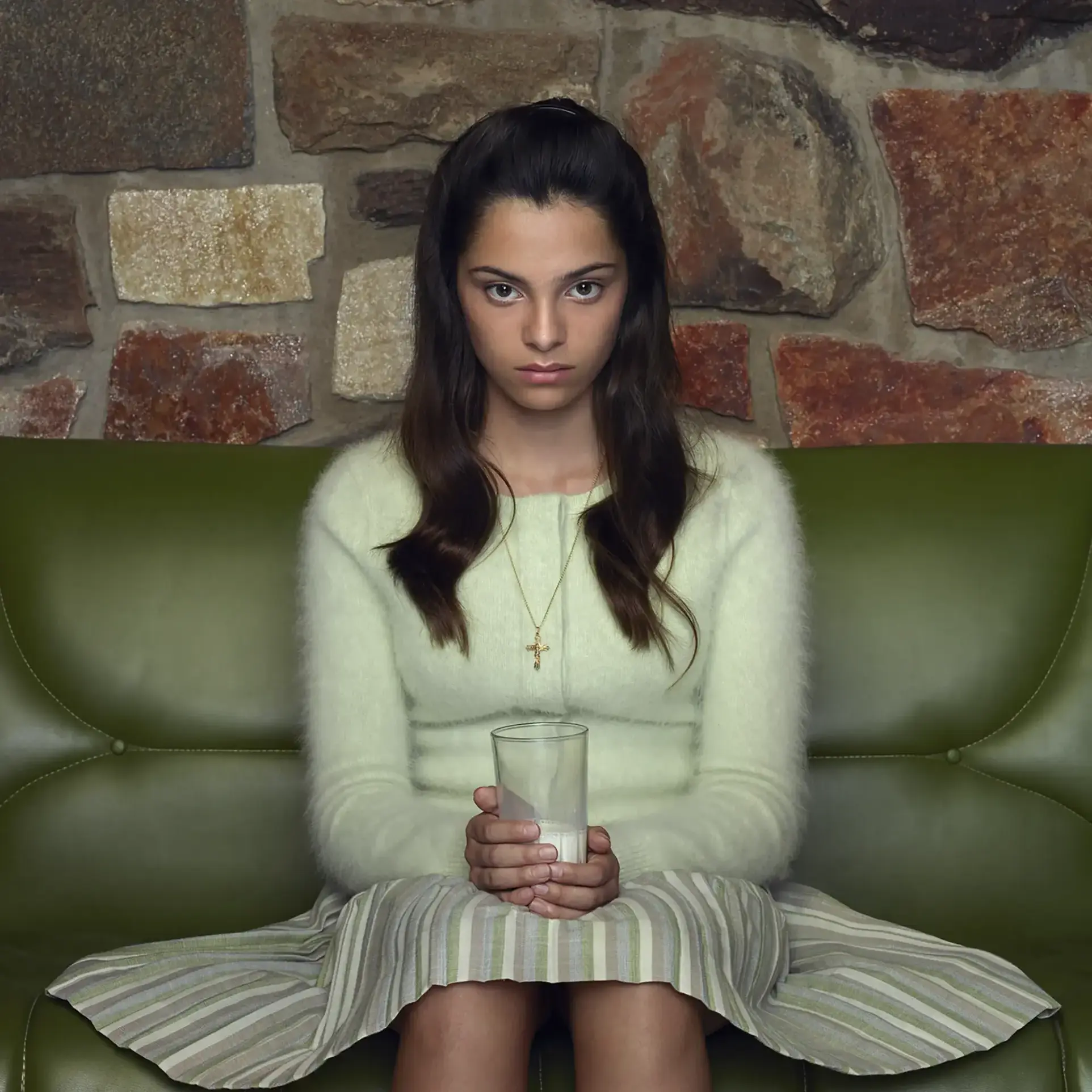 Meisje zittend op een groene bank met een glas melk in haar handen.